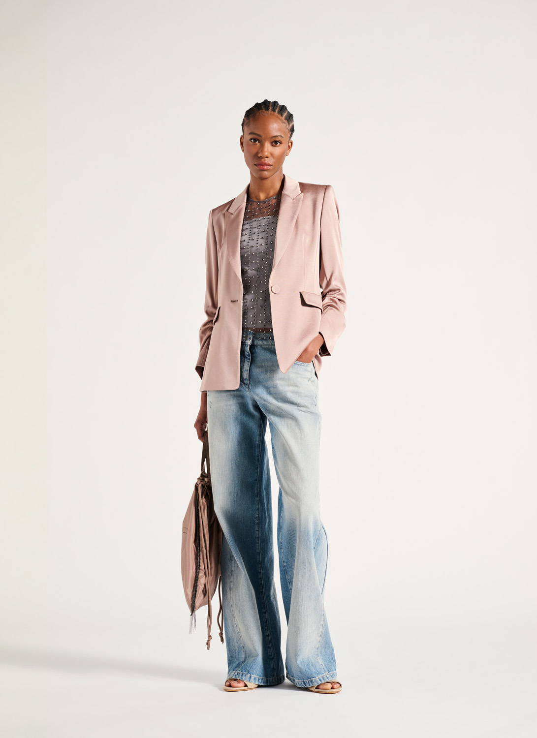A model in Luisa Cerano brand clothing a light pink blazer with casual jeans stands against a white wall.